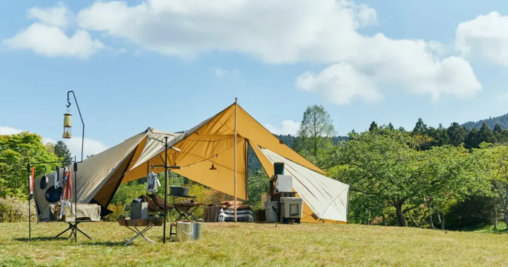 自然の中に設営された大型テントとキャンプ道具の風景